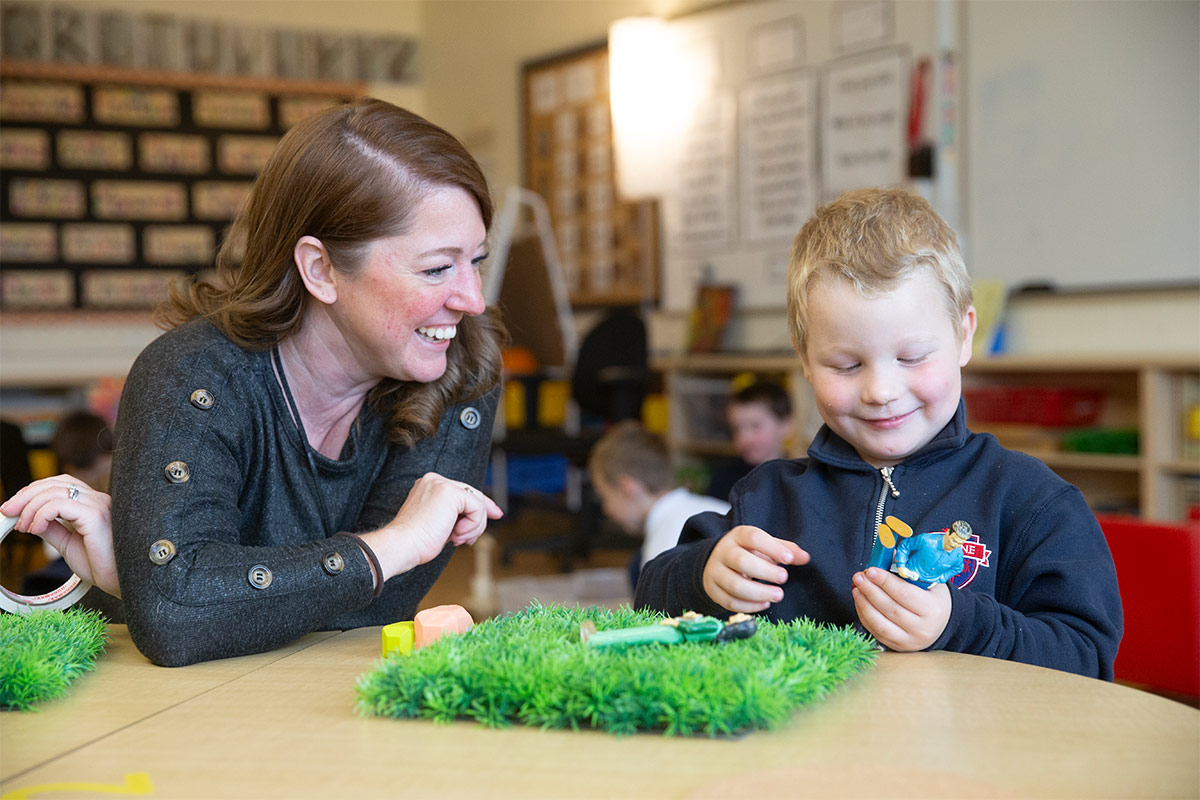 Female kindergarten teacher with young male student, interacting and smiling