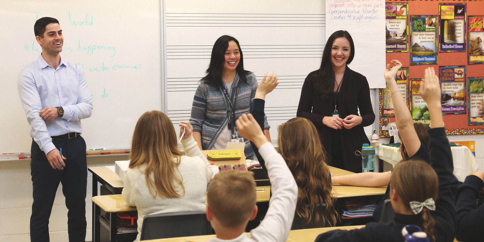 Classroom teacher, School Principal, and EA standing in front of an elementary classroom of children with their arms raised